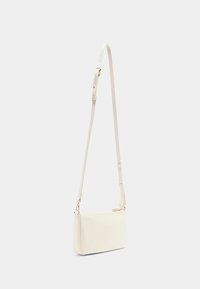 Sac bandoulière en similicuir blanc avec un design mince, une bandoulière réglable et des accessoires dorés. Surface texturée avec une fermeture éclair.