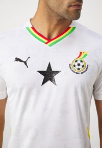 Hvid fodboldtrøje med et sort stjernedesign, grøn, rød og gul krave samt Puma-logo. Fungerer med Ghana Football Associations insignia.