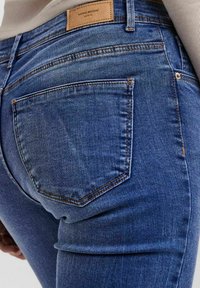 Jeans de mezclilla azul oscuro con una textura suave, que presentan un bolsillo trasero y una etiqueta de cuero con la marca en la cinturilla.