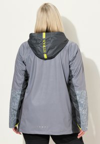 Veste imperméable grise avec capuche, dotée d'accents jaunes, motif floral sur les manches et texture lisse. Vue de dos affichée.