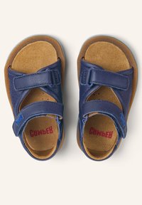 Sandali in pelle blu con fasce in Velcro e soletta in camoscio marrone, dotati di suola in gomma azzurro chiaro. Testo "Cwber" stampato in rosso.