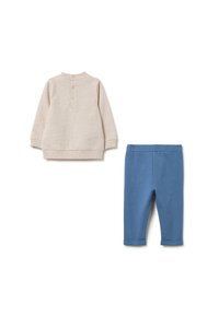 Lichtbeige langemouwen top met een sluiting met knopen aan de achterkant en blauwe stretchbroek, beide gemaakt van een zachte stof. De broek heeft opgerolde manchetten.