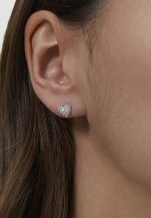 Orecchino a bottone a forma di cuore in argento con superficie testurizzata e scintillante. Inquadratura ravvicinata dell'orecchio e dei capelli.