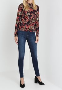 Maglietta nera a maniche lunghe con un motivo floreale colorato, abbinata a jeans skinny blu scuro e scarpe con tacco nere.