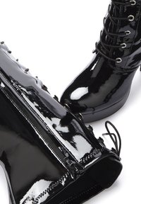 Black patent leather ankle boots with a high heel, featuring lace-up design, metallic eyelets, and a side zipper for closure.