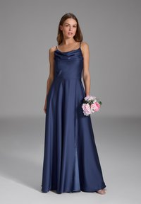 Robe en satin marine avec un décolleté drapé, des bretelles spaghetti et une jupe fluide. Le modèle tient un bouquet de fleurs roses.