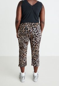 Pantalons courts à imprimé léopard avec une taille haute, présentant un mélange de marron, noir et touches de rouge, associés à un débardeur noir.