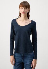 Long-sleeve navy v-neck shirt made of soft fabric, featuring a relaxed fit and smooth texture. Worn with blue denim jeans.