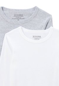 Deux t-shirts empilés. L'un est gris clair, l'autre est blanc. Les deux ont des encolures rondes et un tissu en coton doux et lisse.
