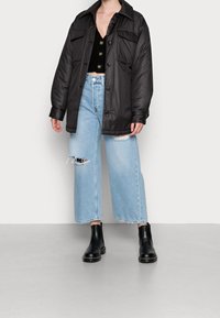 Chaqueta acolchada negra con grandes botones, combinada con unos vaqueros anchos desgastados de color azul claro y botas de tobillo negras.