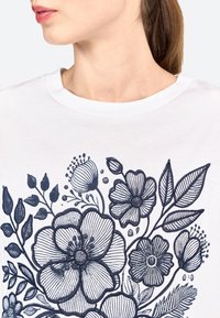 Witte t-shirt met een marineblauwe floral illustratie van verschillende bloemen en bladeren, met gedetailleerd lijnwerk en een ronde halslijn.