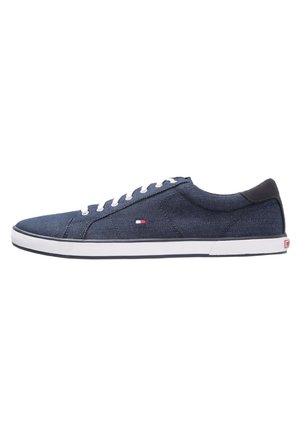 Baskets basses en toile bleu marine avec des lacets blancs, une semelle blanche et un petit logo rouge, blanc et bleu sur le côté.