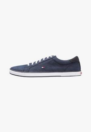 Zapatilla baja de lona azul marino con cordones blancos, suela blanca y pequeño logo rojo, blanco y azul en el lateral.