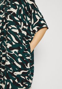 Luźna sukienka w czarnym, niebieskawym i kremowym abstrakcyjnym wzorze; krótkie rękawy, boczne kieszenie, wykonana z gładkiego materiału.