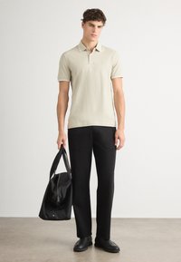 Polo beige avec des détails contrastants au niveau du col, pantalon noir et sac de sport noir. Tissu lisse, coupe ajustée et design minimaliste.