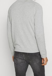 Szary bawełniany sweter z okrągłym dekoltem, ściągaczami na rękawach i dole, pokazany od tyłu, w zestawieniu z ciemnymi jeansami. Brak widocznych wzorów lub dodatków.