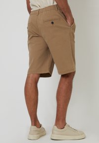 Braune Baumwollshorts mit elastischem Bund, seitlichen Taschen und einer Gesäßtasche mit Knopfdetails. Lässige Passform und knielanges Design.