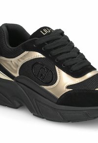 Sneakers neri con dettagli metallici dorati, materiali in rete e suede, suola in gomma testurizzata e dettaglio del logo sul lato.