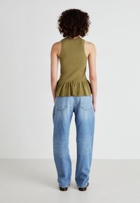Top sin mangas de canalé en verde olivo con un dobladillo peplum, combinado con jeans de pierna ancha en azul claro. Muestra un ajuste casual y relajado sin logotipos visibles.