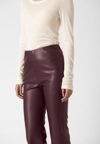 Bluză crem cu mânecă lungă și decolteu rotund, asociată cu pantaloni din piele burgundy, având o textură fină și un design cu talie înaltă.