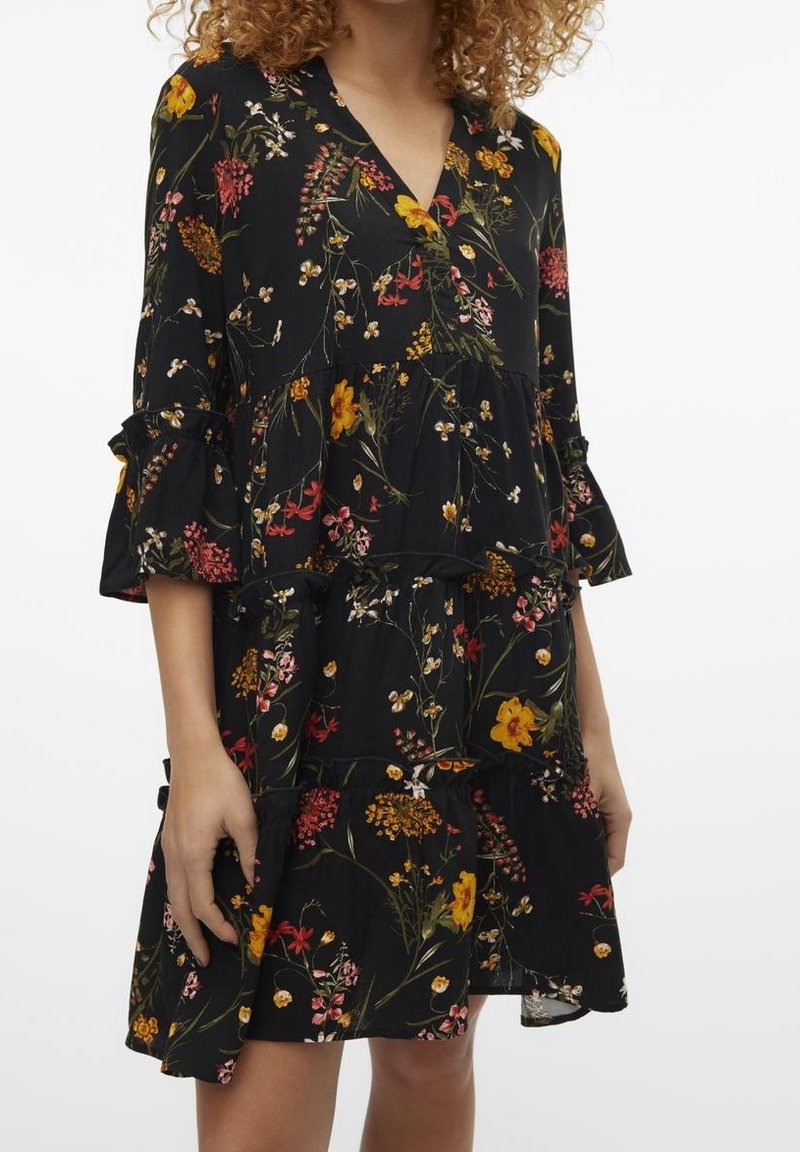 Robe fleurie noire à volants avec un design à étages, manches volantées et motifs floraux colorés en rouge, jaune et blanc. Tissu léger.