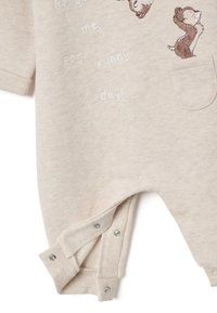 Hellbeige Einteiler aus weichem Stoff, mit kurzen Ärmeln, einer Tasche, gestickten Tiersymbolen und Druckknöpfen am Boden.