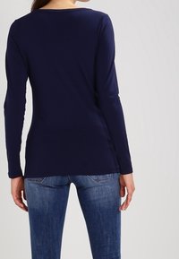 Marinblå långärmad topp med rundad halsringning och mjuk yta, i kombination med blå jeans, som visar en figurnära silhuett och avslappnad design.