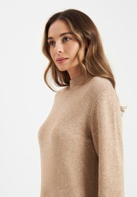 Strickpullover mit Rollkragen in Beige. Weicher, strukturierten Stoff mit lockerer Passform und langen Ärmeln. Nahtdetails an den Schultern.