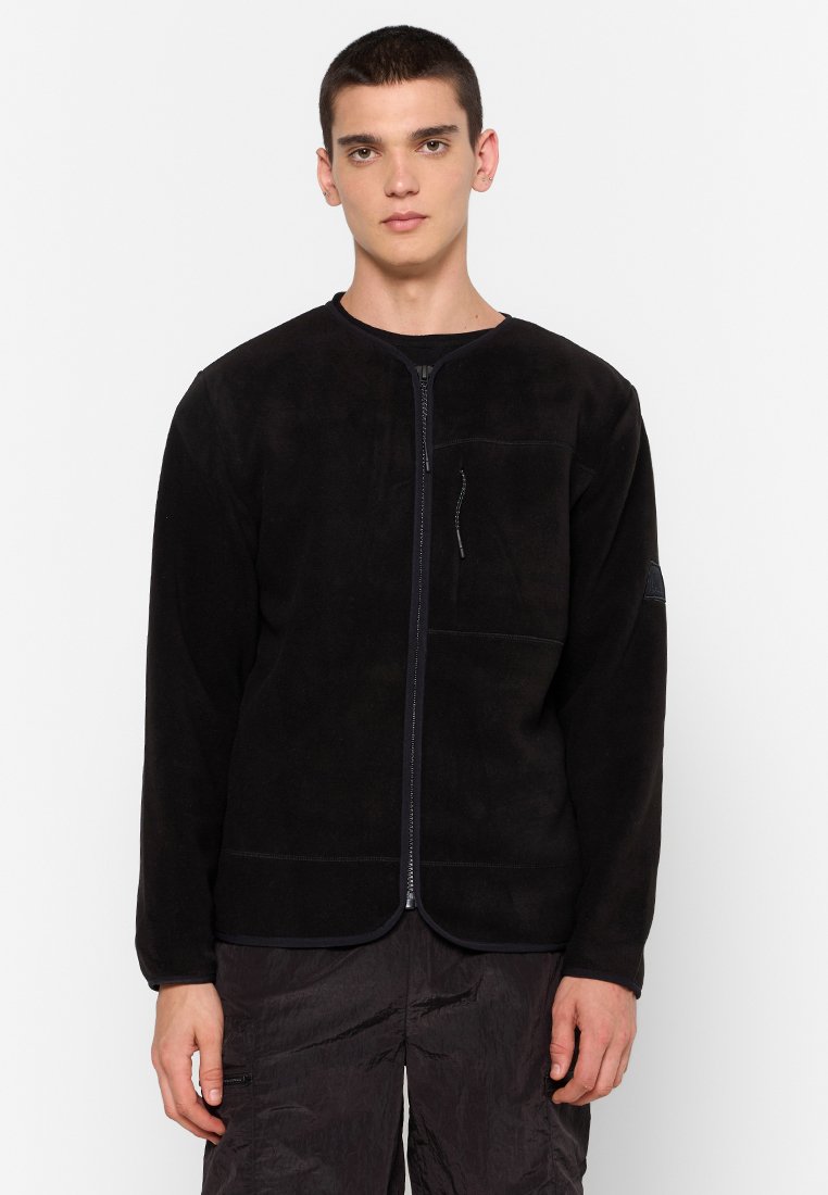 Giacca in pile nera con scollatura rotonda, chiusura frontale con zip e tasca laterale. Il tessuto ha una texture liscia con dettagli cuciti.