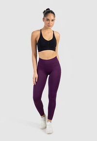 Schwarzer Sport-BH und hoch taillierte lilafarbene Leggings, getragen mit weißen Sneakers. Glatter Stoff, figurbetontes Design und minimalistische Details.