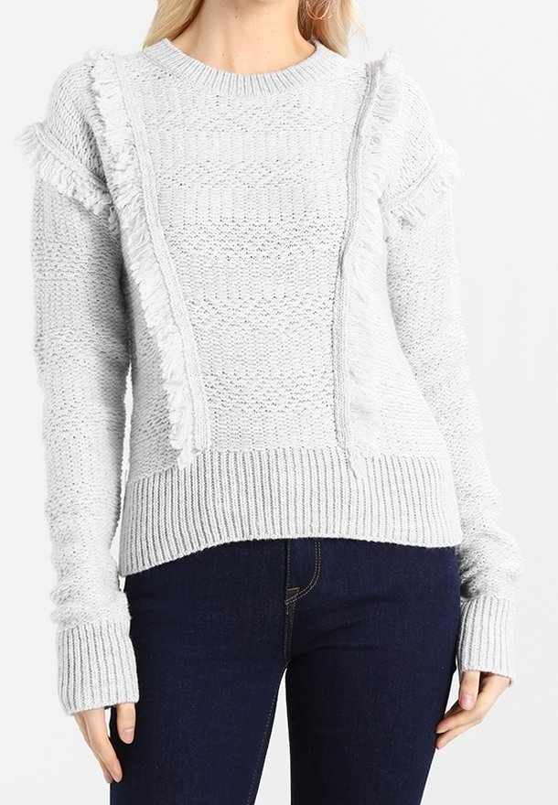 Jasnoszary sweter dziergany z teksturowymi panelami, frędzlami wzdłuż szwów na ramionach oraz ściągaczami na mankietach i dole.
