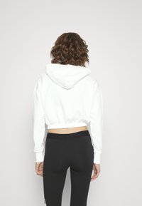 Felpa bianca corta con cappuccio regolabile, orlo elasticizzato e maniche lunghe, abbinata a leggins neri attillati.