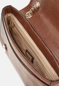 Borsa a tracolla marrone con texture in rilievo a motivo rettile, hardware dorato e dettaglio in catena. L'interno include un logo e una tasca con zip.