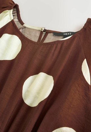 Ruda audinio palaidinė su didelėmis kreminėmis taškelėmis, su apvalia iškirpte ir užpakalinį raktelio formos plyšį. Medžiaga turi lygią faktūrą.