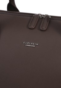 Sötétbarna bőr táska dupla cipzárhúzóval és ezüst "Carlheim Copenhagen" logóval, amely a cipzár alatt középen helyezkedik el.