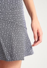 Zwart-witte rok met een patroon, voorzien van een uitlopende pasvorm, gestructureerde stof en een tailleband met diagonaal geplaatste panelen.