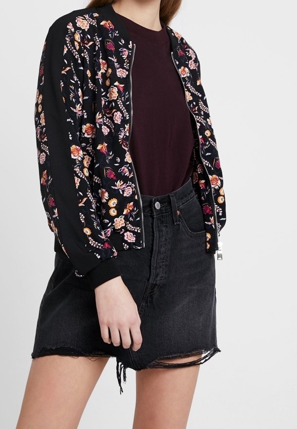 Blomster bomberjakke i sort stof med flerfarvede blomstermønstre, parret med en burgunder top og en slidte denimnederdel i sort.