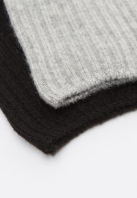 Deux écharpes en tricot pliées, une gris clair et une noire, avec une texture côtelée sur une surface blanche.