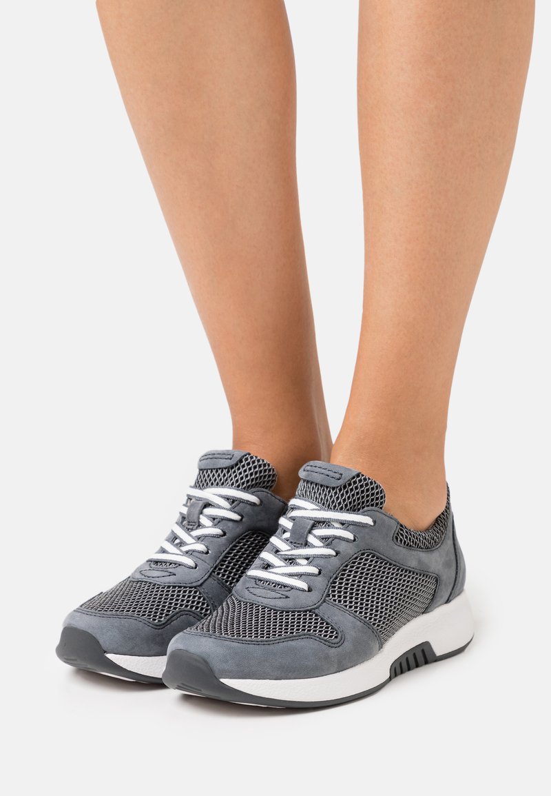 Graue Sportschuhe mit Mesh-Einsätzen, Wildlederakzenten, weißen Schnürsenkeln und einer dicken weißen Sohle. Das Design ist ein Low-Top-Modell mit gepolstertem Kragen.