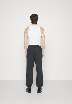 Pantalones negros, holgados, con puños elásticos, llevados sobre una camiseta sin mangas blanca. El material parece suave y tiene bolsillos en la parte posterior.
