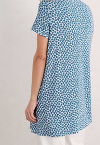 Sininen kukkakuosiset tunikapaita lyhyillä hihoilla ja löysällä istuvuudella. Valmistettu kevyestä kankaasta, jossa on ympyräkaula-aukko ja sivuhalkiot.