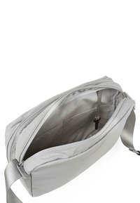 Bolso cruzado de tela gris con una textura suave, compartimento principal con cremallera y correa ajustable. El interior tiene bolsillos para la organización.