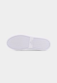 Λευκή σόλα αθλητικού παπουτσιού με μοτίβο ανάγλυφης οδοντωτής γραμμής και την επωνυμία "Lacoste" καθώς και το λογότυπο του κροκόδειλου στην περιοχή της καμάρας.