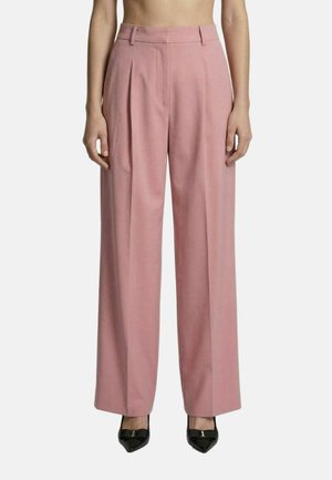 Pantaloni rosa a gamba larga indossati da una persona in piedi, abbinati a décolleté nere con punta a punta, su uno sfondo bianco uniforme.