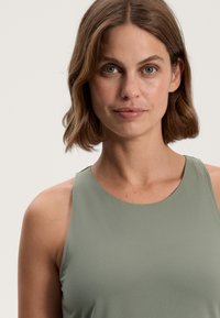 Light olive-green sleeveless top with a round neckline, smooth texture, and fitted design, showcasing a simple and clean aesthetic.