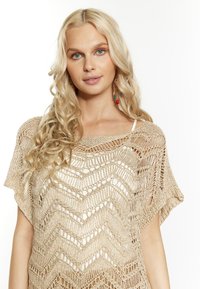Top de ganchillo beige con un patrón de zigzag, con mangas cortas y un escote amplio, hecho de un material ligero y texturizado.