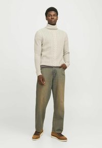 Suéter de cuello alto de punto trenzado en gris claro, jeans holgados azules y zapatos de cordones en color beige. El suéter presenta patrones texturizados y puños acanalados.
