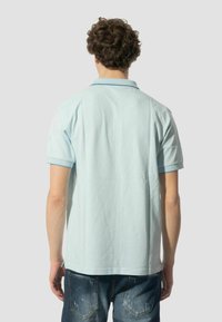 Polo shirt azzurro chiaro con maniche corte, colletto e bordature a contrasto. Indossato con jeans in denim scuri con dettagli sfilacciati.