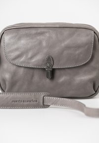 Borsa a tracolla in pelle grigia con una texture liscia, chiusura a patta e cuciture sottili; presenta una tracolla brandizzata e hardware minimal.