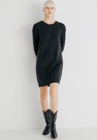 Vestido preto de malha com mangas longas, decote redondo e um ajuste solto, combinado com botas pretas até ao joelho. Textura suave, design minimalista.